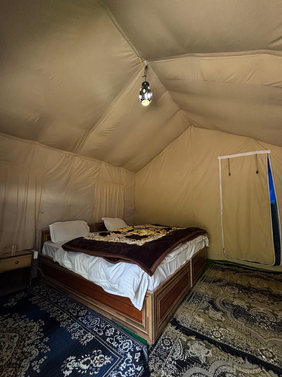 Swiss tent interior: double bed with ethnic carpet and pendant lantern