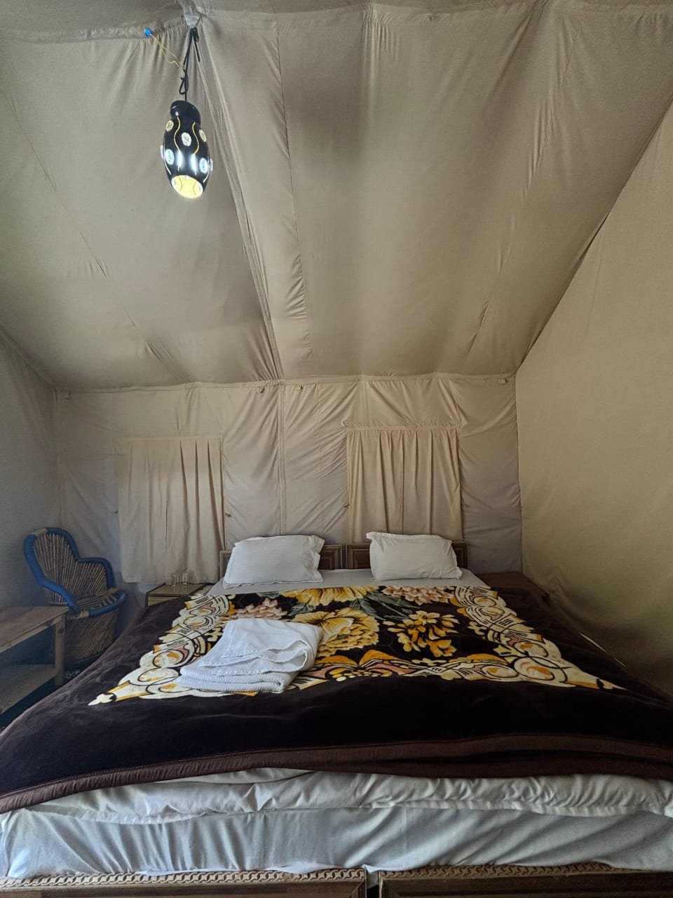 Swiss camp tent interior: double bed with floral quilt, folded towels, pendant lamp
