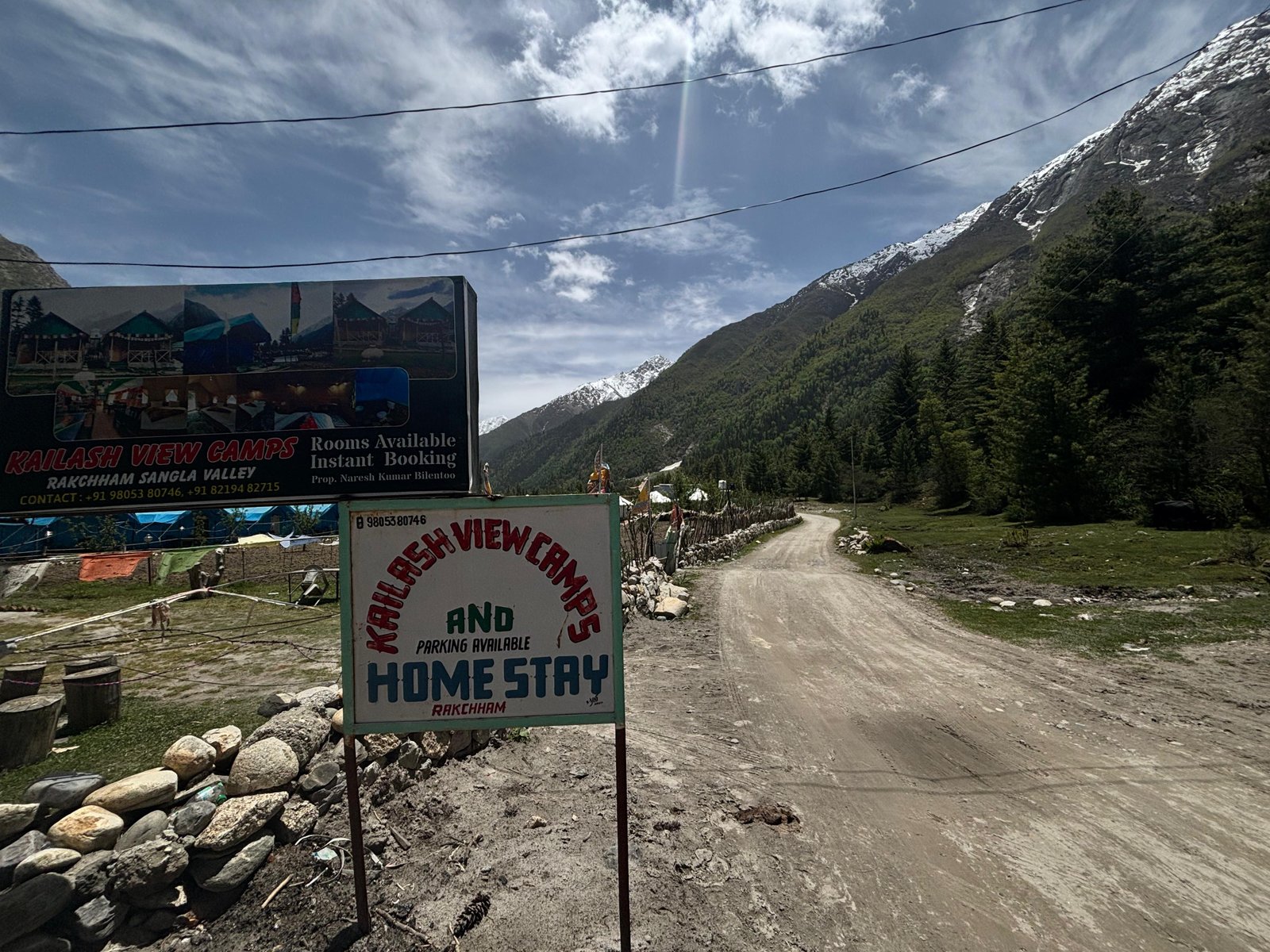 Mountain road leading to Kailash View Camps sign with the Sangla Valley peaks behind